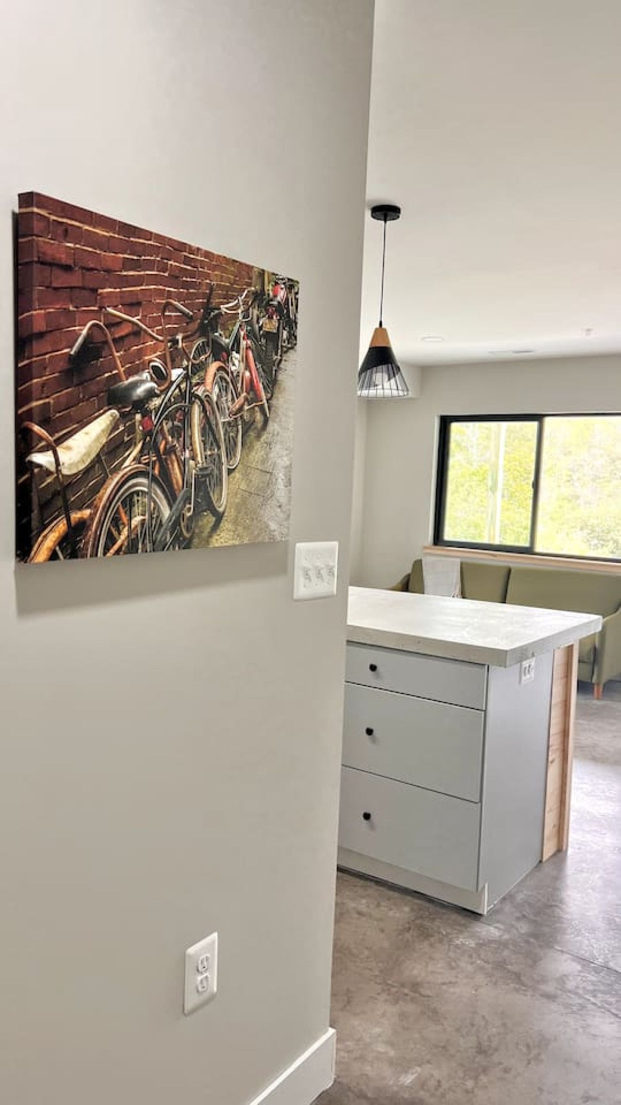 A room with a kitchen island, a wall-mounted bicycle painting, and a pendant light.