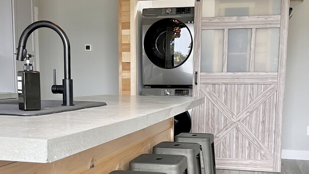 Une cuisine équipée d’un lave-linge intégré, un coin bar avec des tabourets et un plafond en bois rustique.