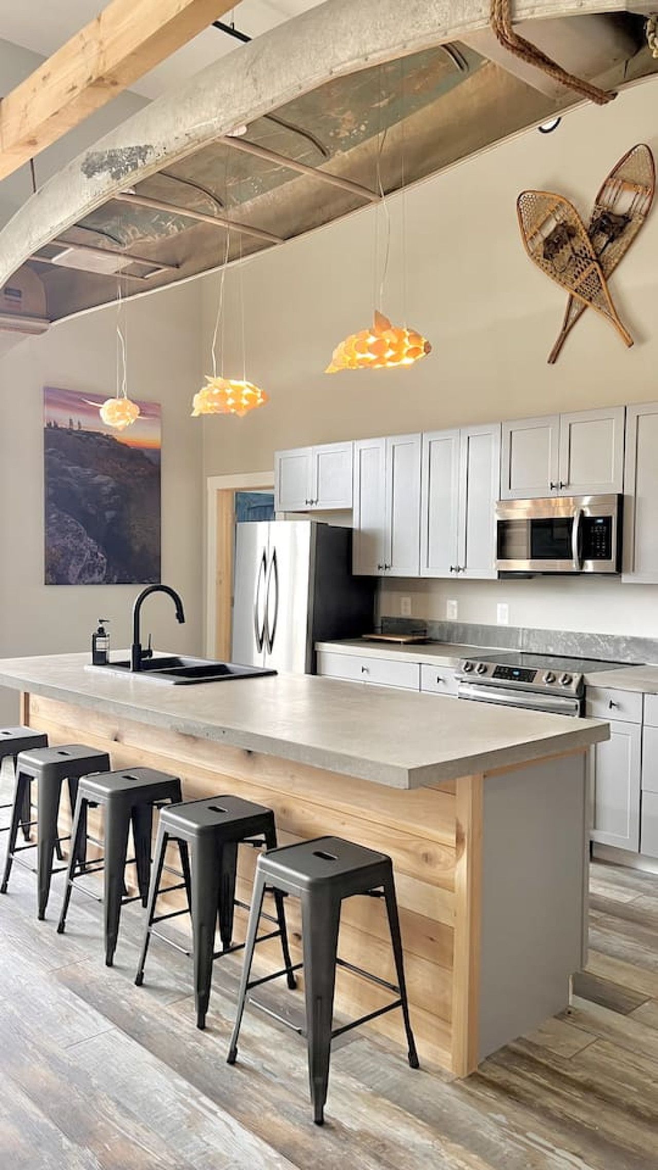 A modern kitchen with a large island, stainless steel appliances, and a rustic ceiling.