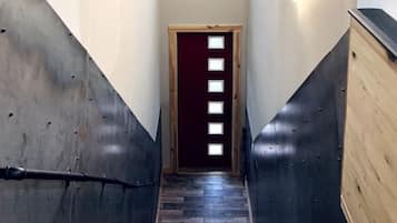 Een smalle trap met een houten leuning, een donker vloerkleed en een deur met een verticale lichtbalk.