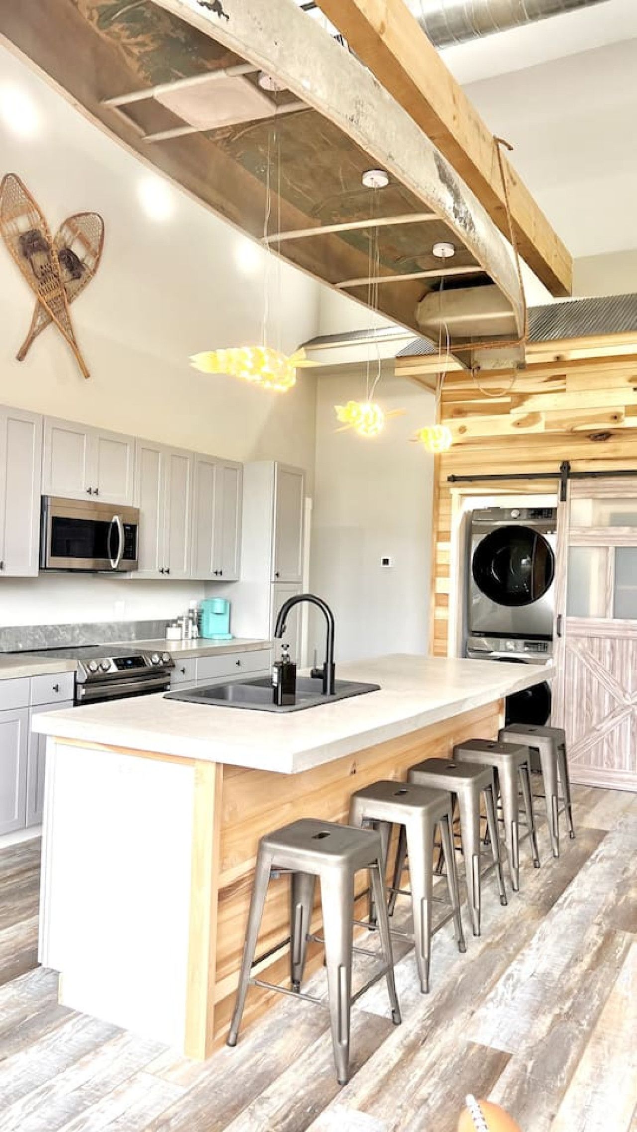 Una cocina moderna con una isla central, taburetes de bar, electrodomésticos de acero inoxidable y vigas de madera a la vista.