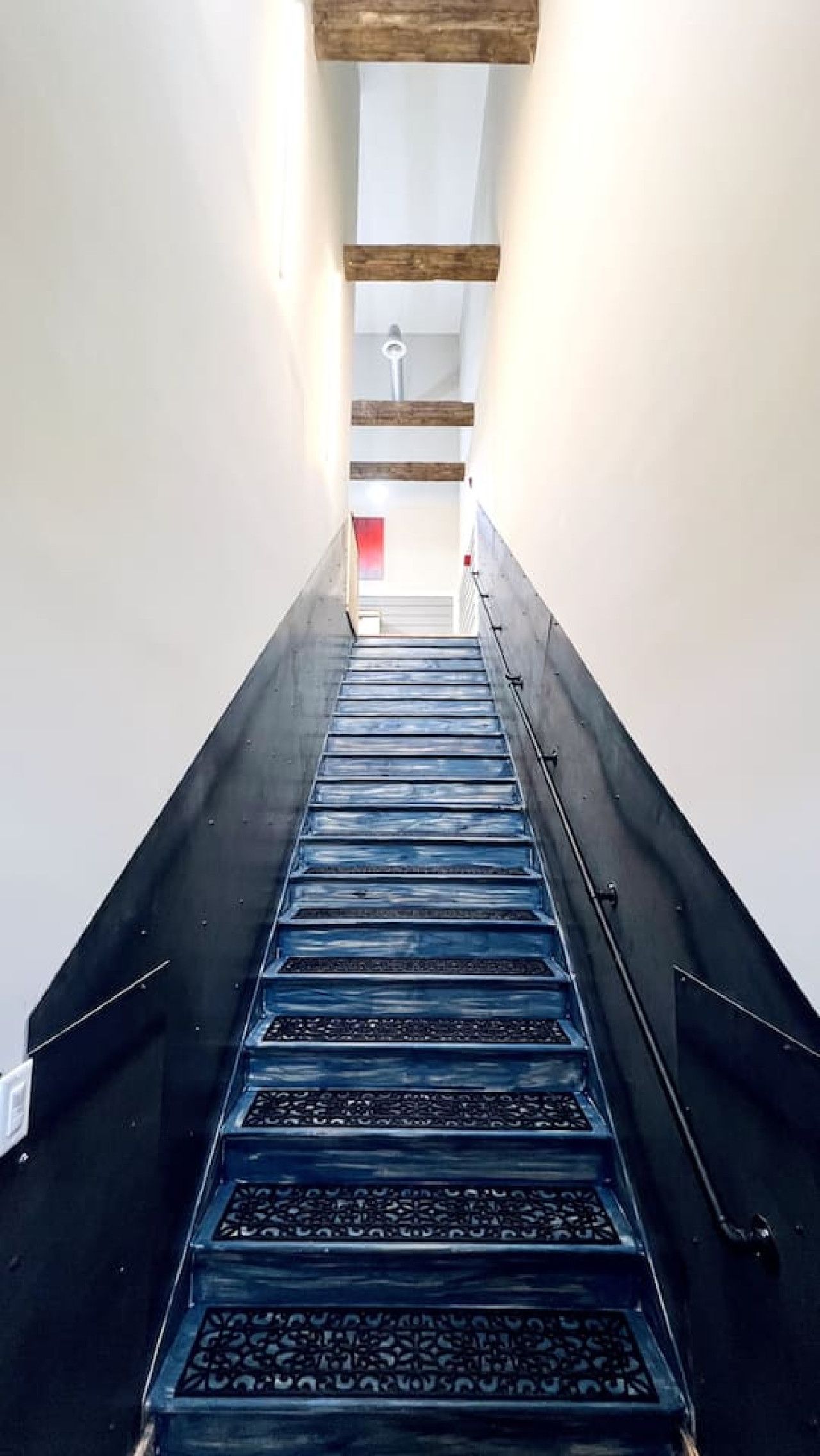 Una escalera estrecha con barandilla en un lado y techo de vigas de madera.