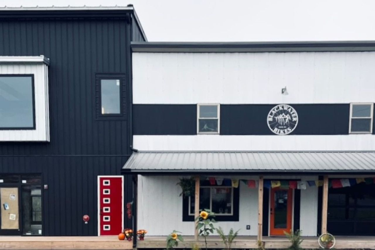 En bygning med en sort-hvid facade, en rød dør og et skilt der står 'Blackwater Bikes'.