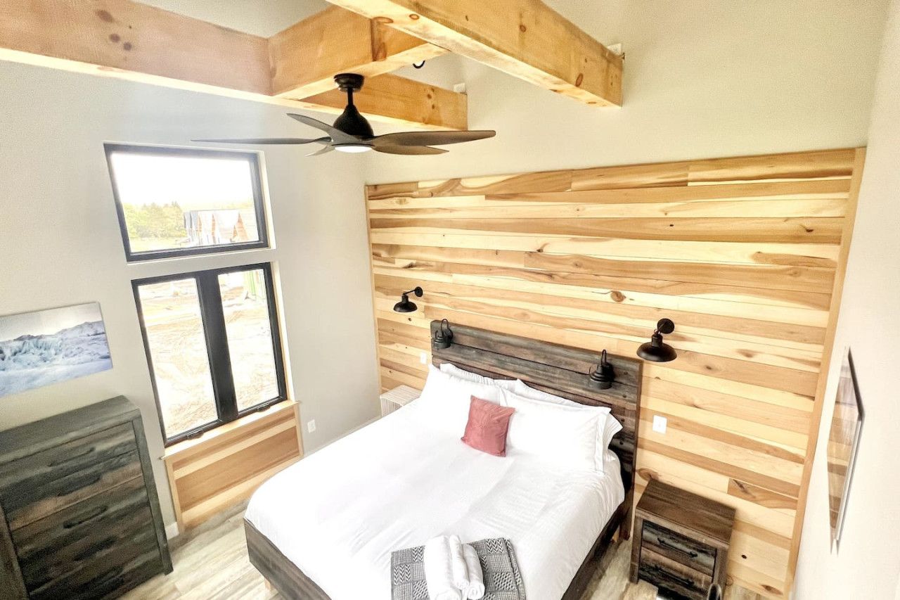 Ein Schlafzimmer mit einem hölzernen Kopfende, einem Bett mit weißer Bettwäsche, einem Deckenventilator und einem Fenster mit Blick.