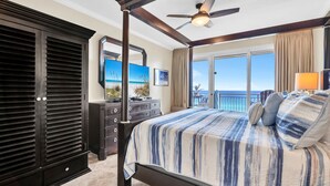 A bedroom with a four-poster bed, a ceiling fan, a large window with a view of the ocean, and a dresser with a mirror. - 🌴 Sterling Shores 908 - Home Sea Home - Gulf Views 🌴 (Destin)