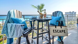 A balcony with two chairs, a small table, and a bag labeled "ESCAPE". - 🌴 Sterling Shores 908 - Home Sea Home - Gulf Views 🌴 (Destin)