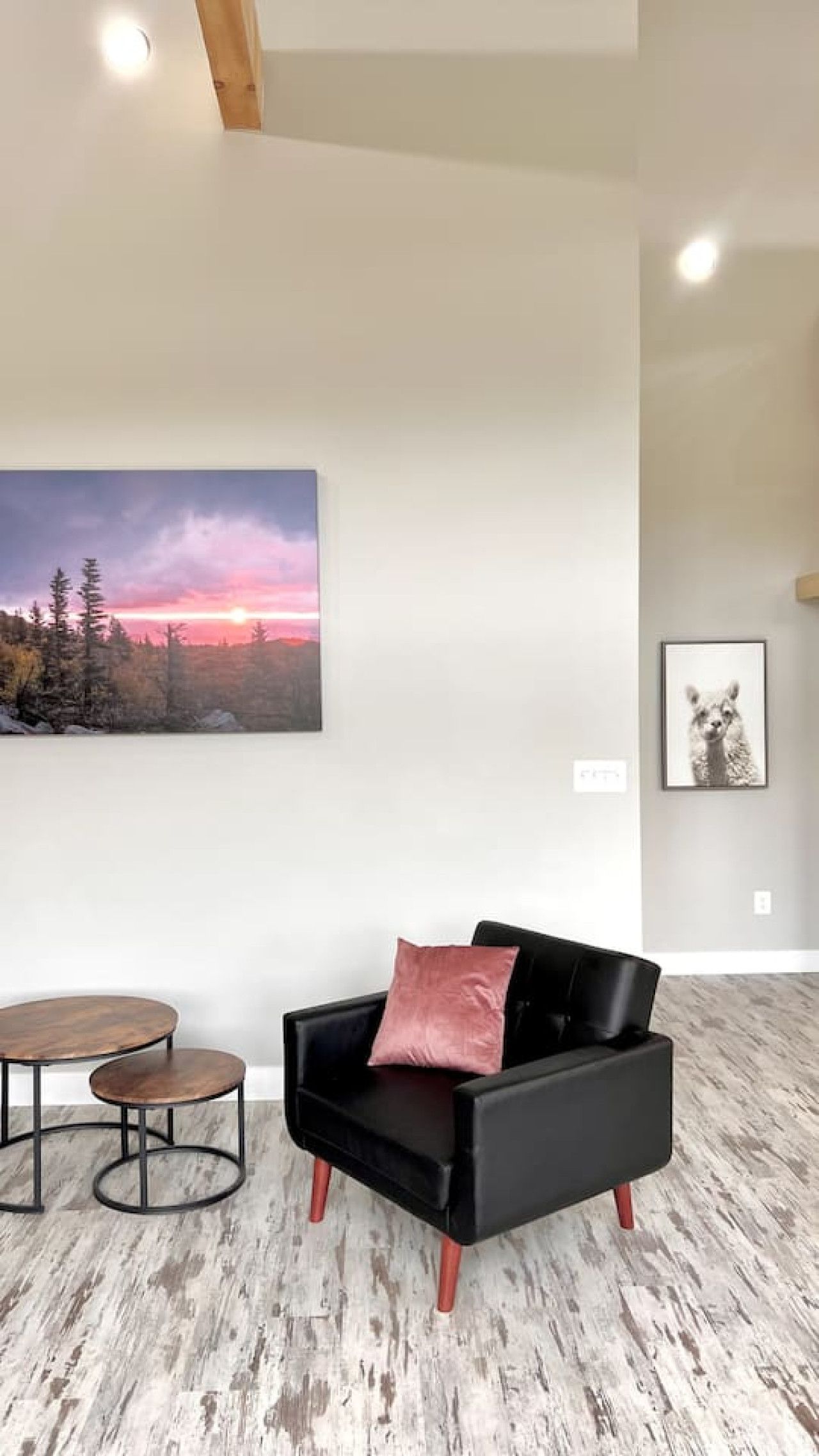 A modern living room with a black leather sofa, a round coffee table, and a painting of a sunset.