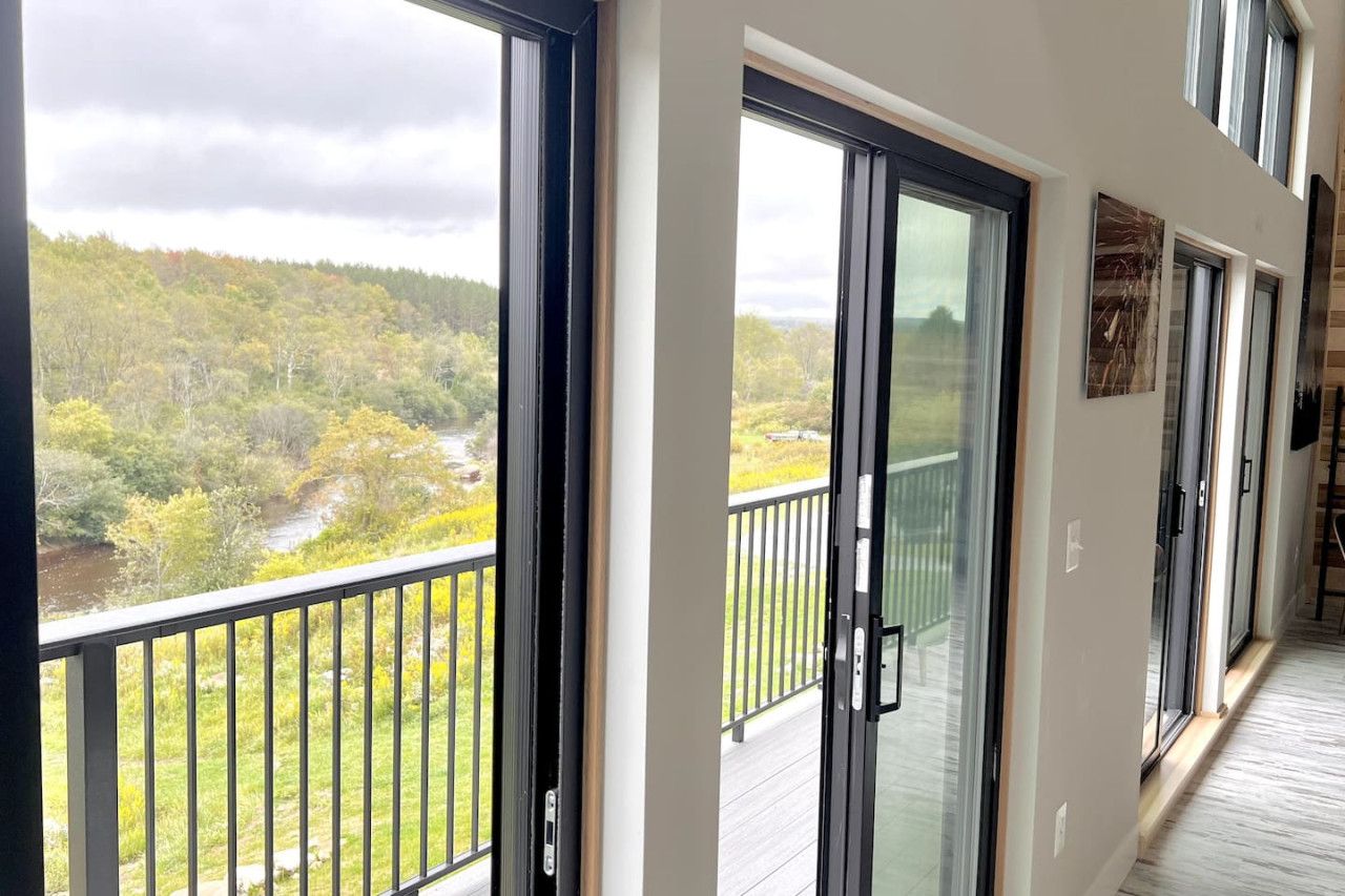 A corridor with large sliding glass doors leading to a balcony with a view of a forested landscape.