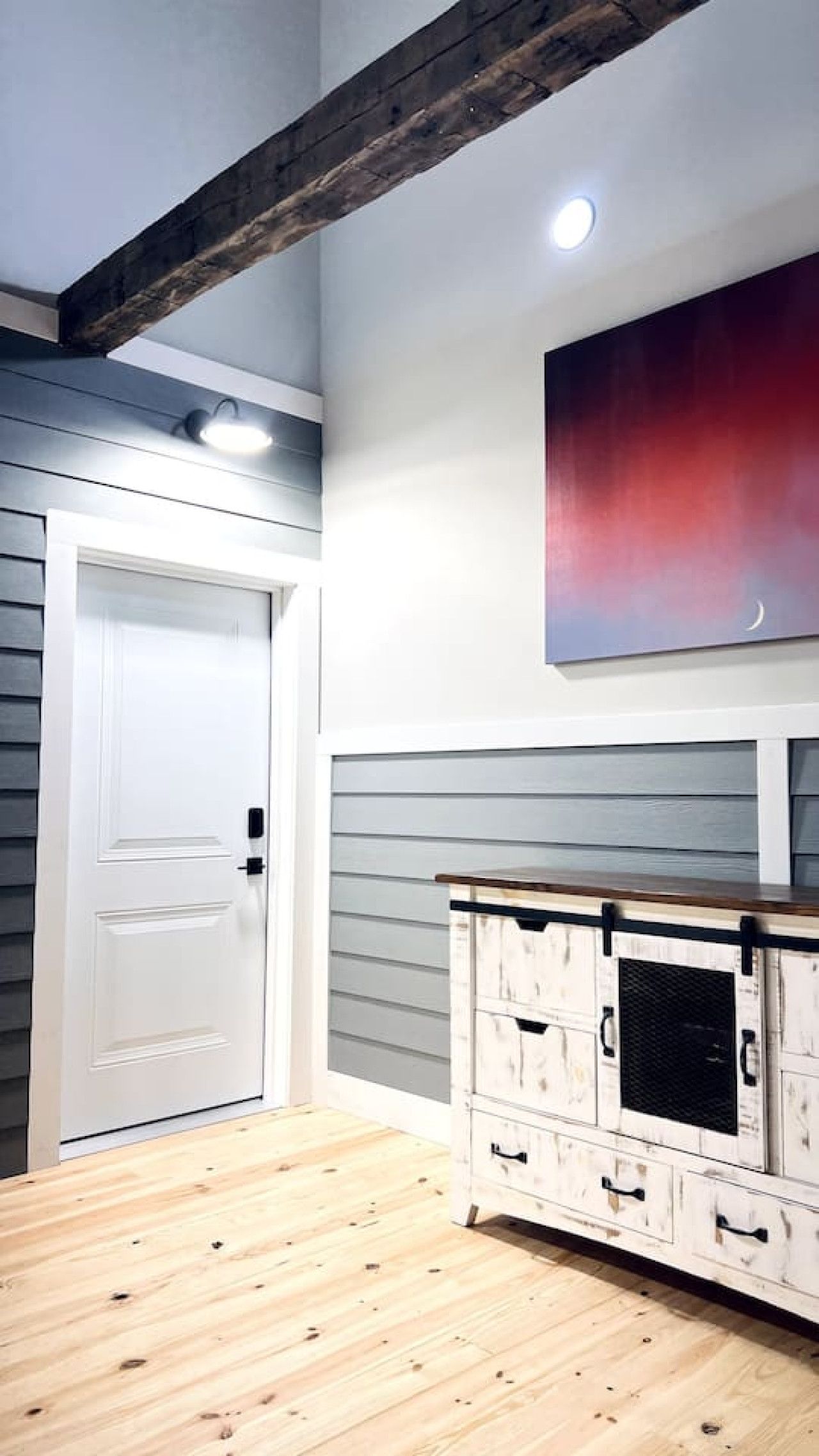 Une pièce avec une porte blanche, un meuble en bois doté de tiroirs et un plafond avec des poutres apparentes.