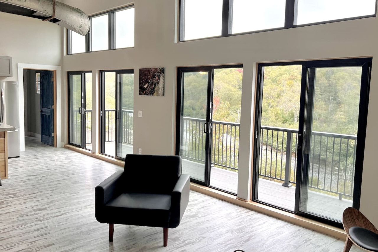 A spacious room with large windows, a black chair, and a view of a balcony.