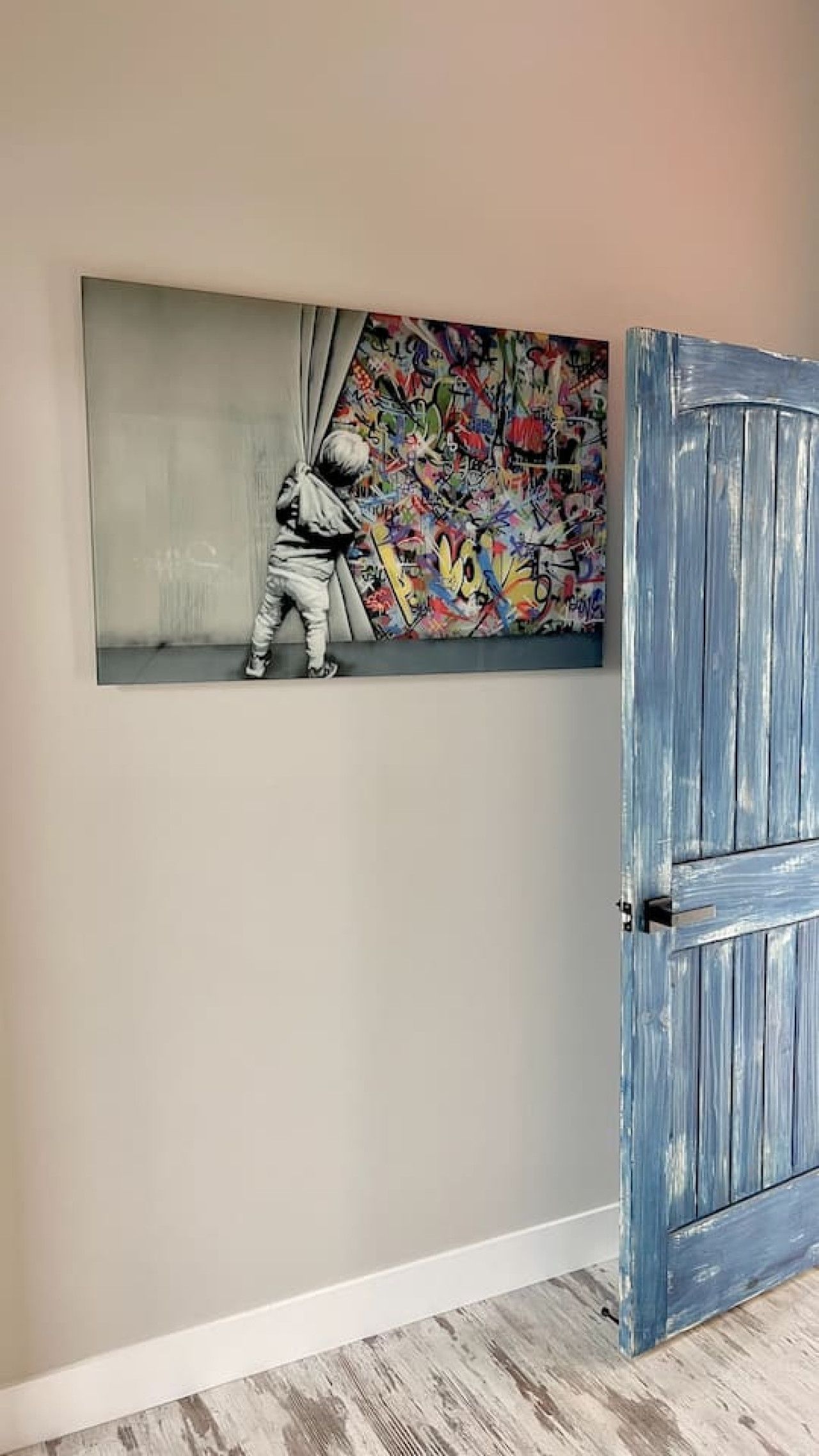 A room with a large abstract painting, a wooden door, and a light-colored floor.