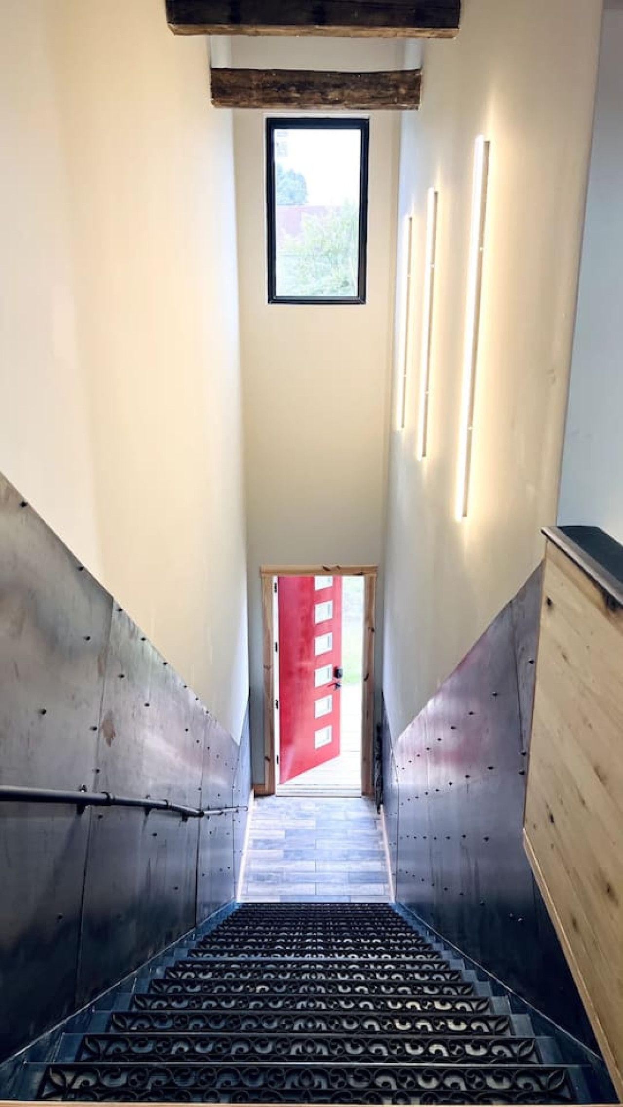 A staircase leading to a red door, with a skylight above and wall-mounted lights.