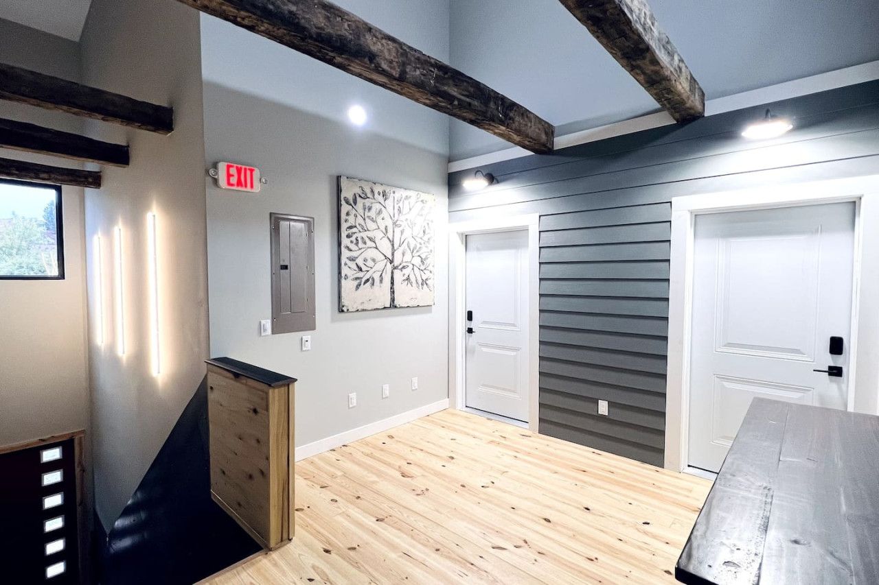Une pièce avec un plancher en bois, un bureau, une commode, une porte et une œuvre d’art accrochée au mur.