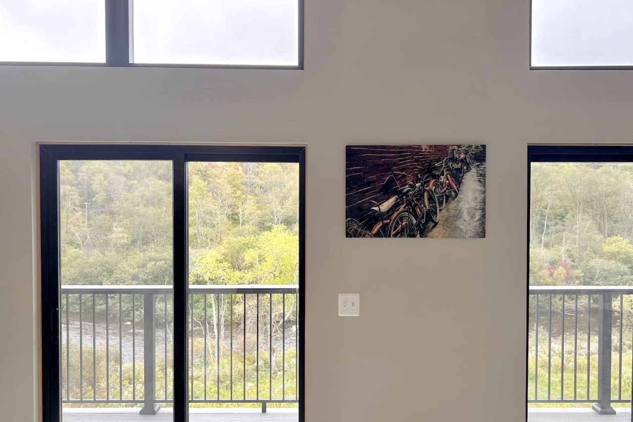 A room with a large window and a painting of bicycles on the wall.