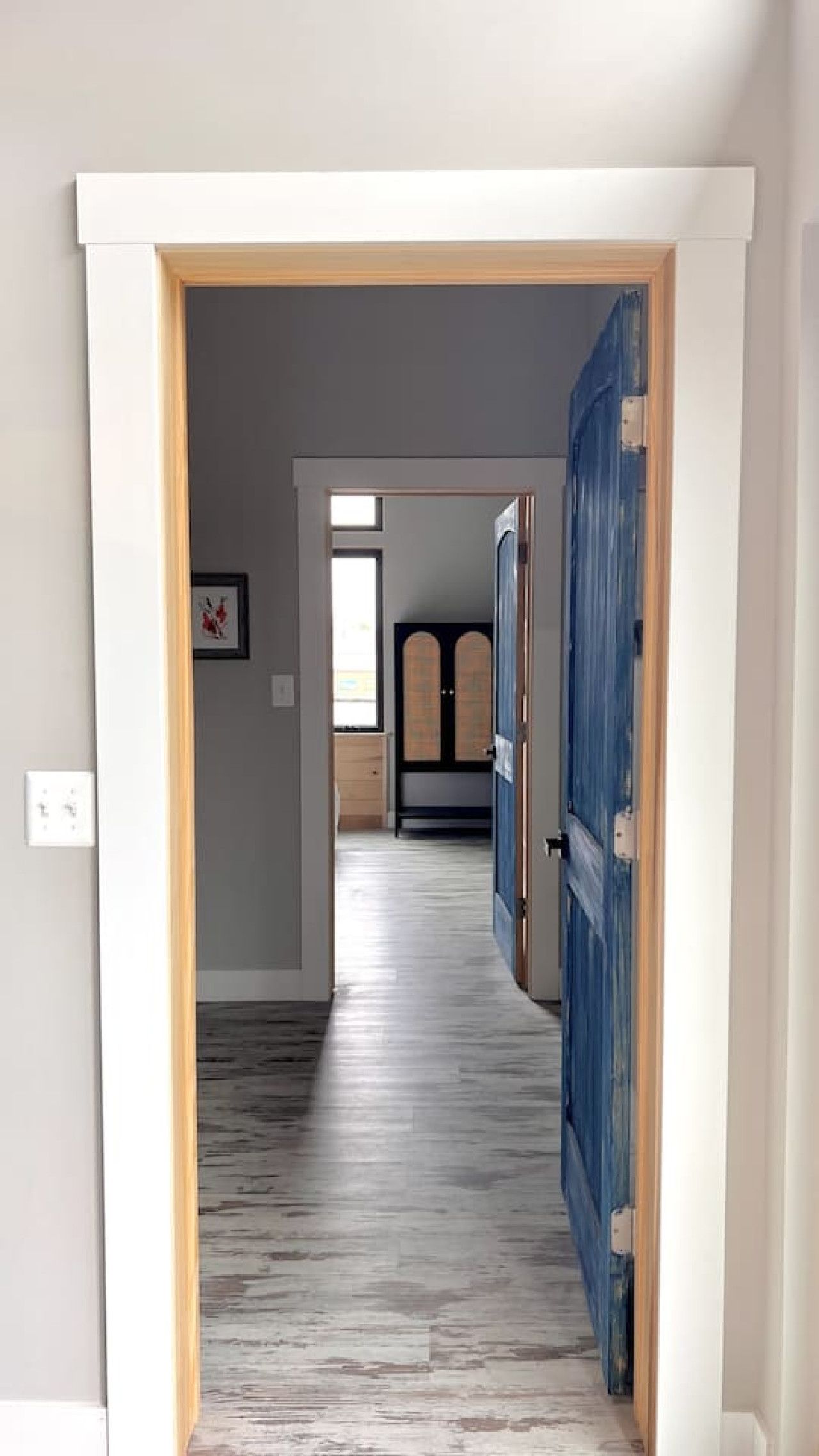 Un couloir au plancher de bois mène à une pièce dont la porte est bleue.
