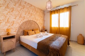 A hotel room with a large bed, a bedside table, a lamp, a window with curtains, and a wall with a leaf pattern.