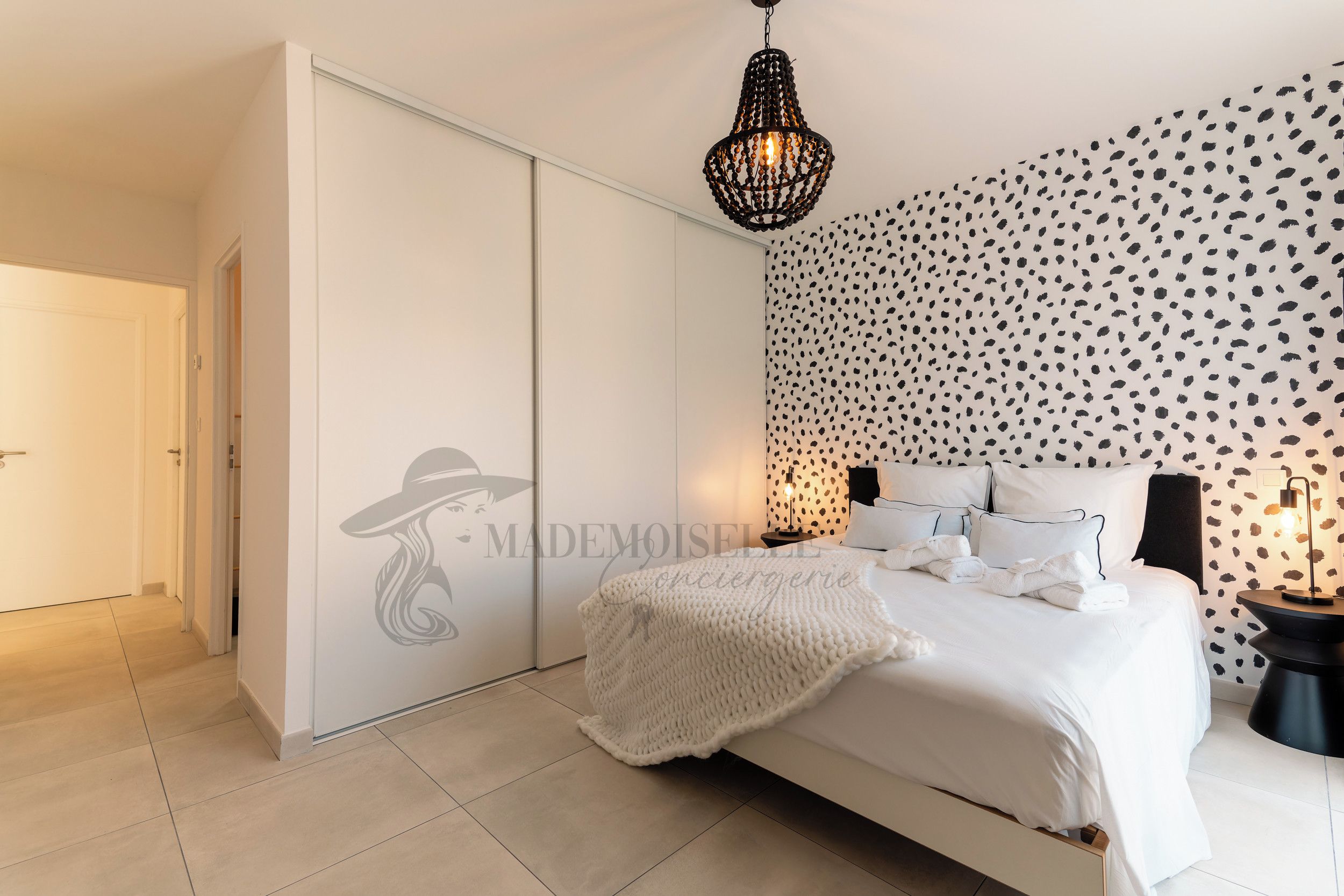 A bedroom with a bed, a wardrobe, a patterned wall, and a hanging light fixture.