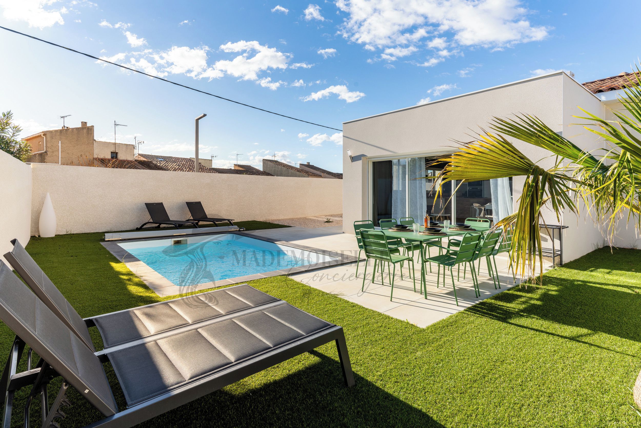 A swimming pool with lounge chairs, a dining area with green chairs, and a small garden with artificial grass.