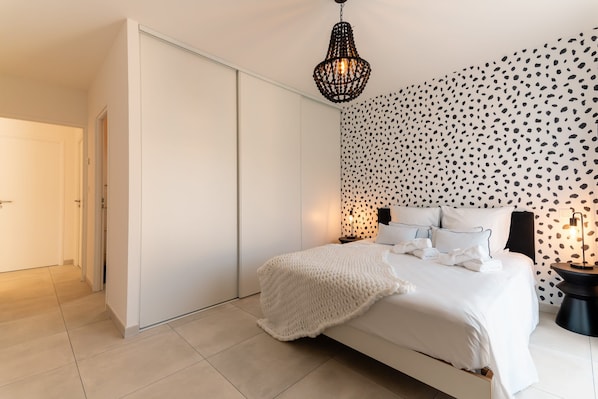 Une chambre à coucher avec un lit, une armoire, un mur à motifs et un luminaire suspendu.