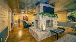 A log cabin interior with a stone fireplace, wooden walls, and a dining area.