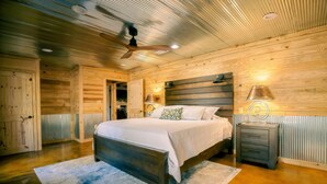A bedroom with a wooden ceiling, a bed with white bedding, a nightstand, and a lamp.