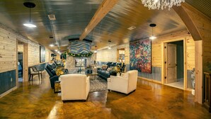 A spacious indoor area with wooden walls and a polished concrete floor. There are several seating areas with leather sofas and armchairs. A large, colorful abstract painting adorns the wall, and a chandelier hangs from the ceiling.