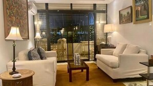 Ein Wohnzimmer mit zwei weißen Sofas, einem Couchtisch und einem Teppich mit Muster. Eine Glastür führt zu einem Balkon mit Stühlen und einem Tisch.