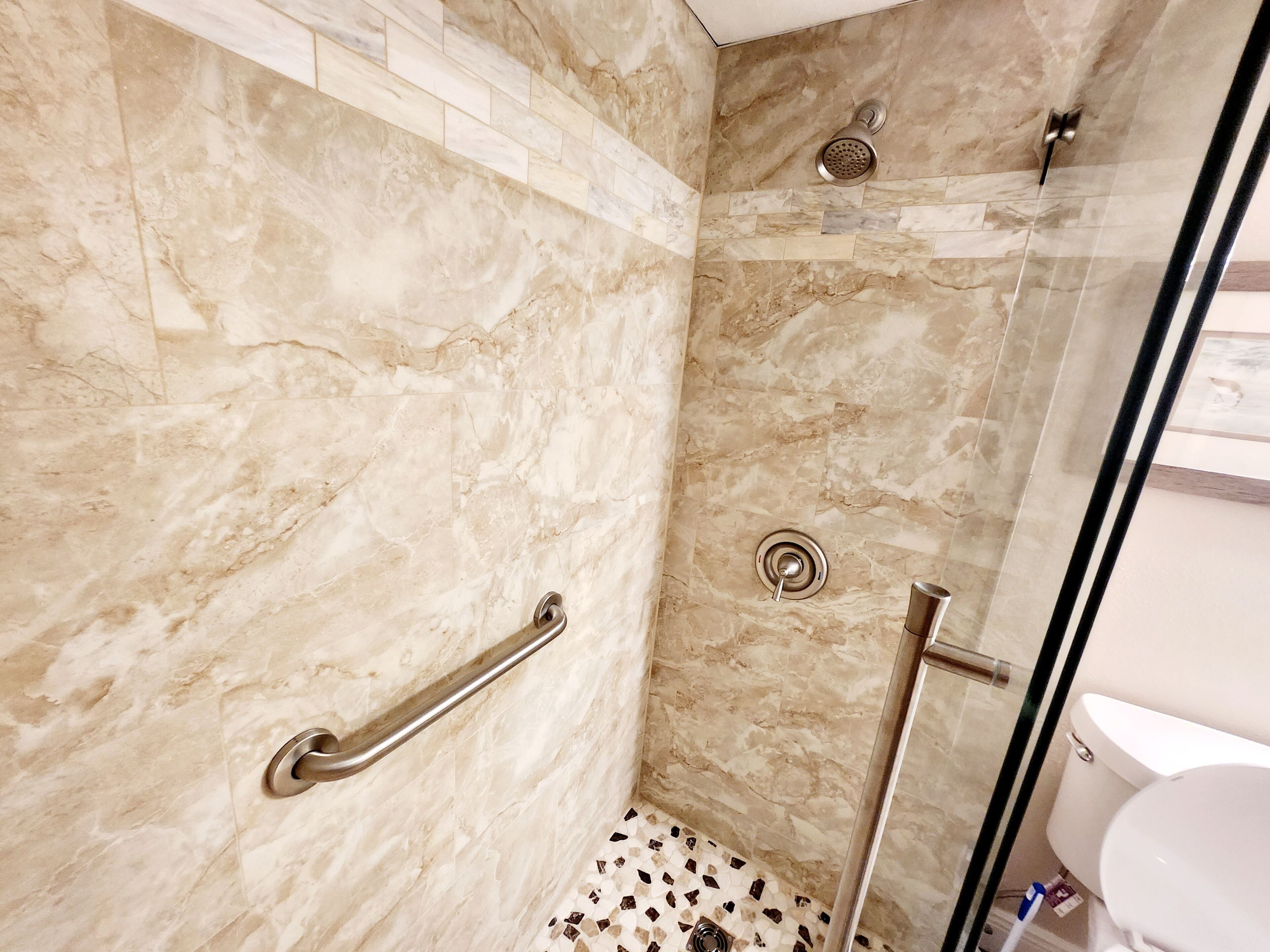 Ein modernes Badezimmer mit Marmorwänden, einer Glasdusche, einer Handstange und einer durch das Glas sichtbaren Toilette.