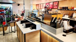 Interior moderno de una cafetería con mostrador, zona de estar y diverso equipo para preparar café.