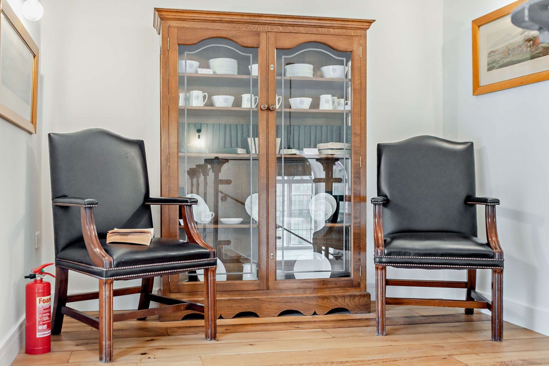 Two black leather chairs with wooden frames and a wooden cabinet with glass doors in the background.