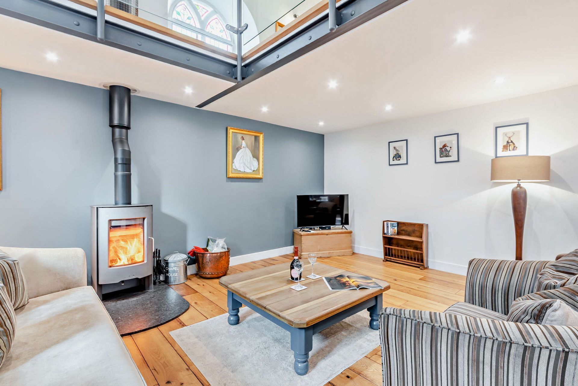 A modern living room with a wood-burning stove, a television, and a loft space above.