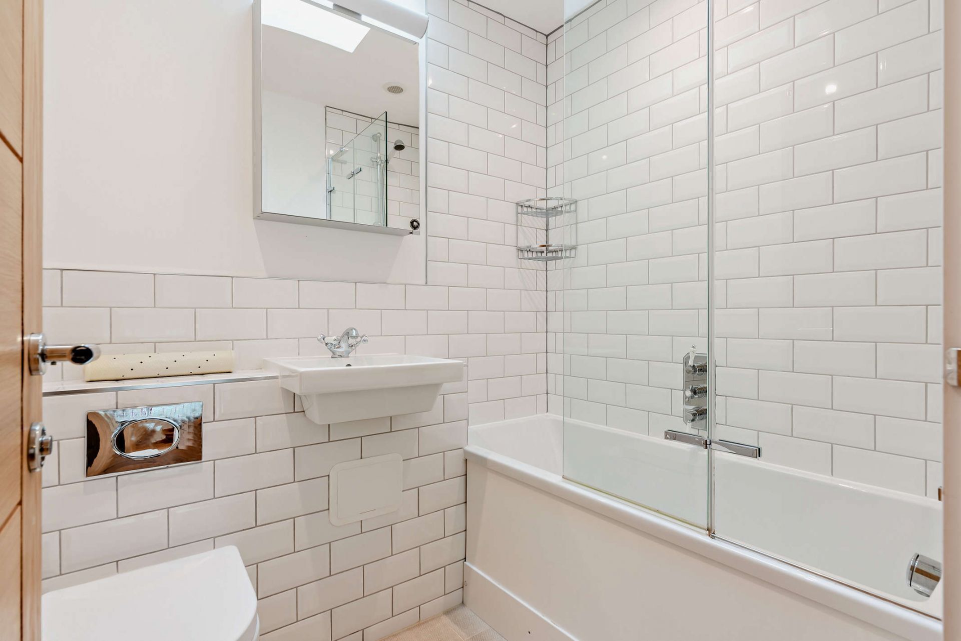 A modern bathroom with white subway tiles, a glass shower enclosure, a white sink, and a toilet.