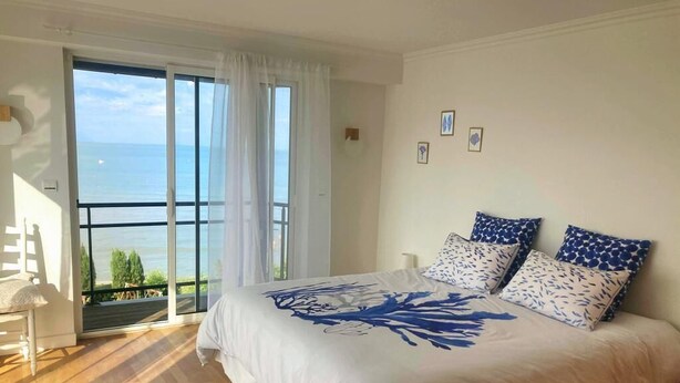 A bedroom with a large bed, a view of the sea through a sliding door, and a balcony.