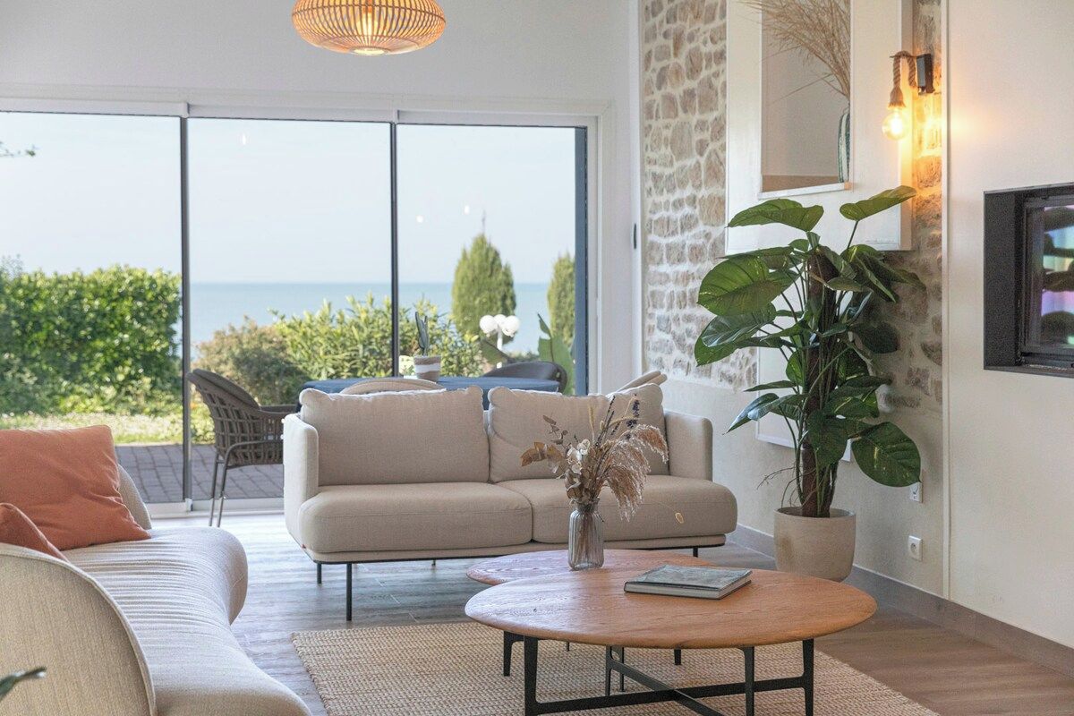 A living room with a sofa, a coffee table, and a potted plant. There is a view of the outdoors through a glass door.