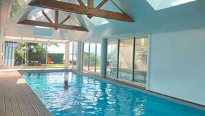 An indoor swimming pool with a wooden deck, large windows, and a skylight.