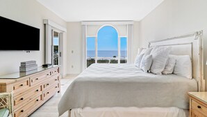 A bedroom with a bed, a dresser, a television, and a view of the sea through a window. - Oceanfront , 3 Bedroom, 3 Bathroom with panoramic ocean views and pool access (Hilton Head Island)