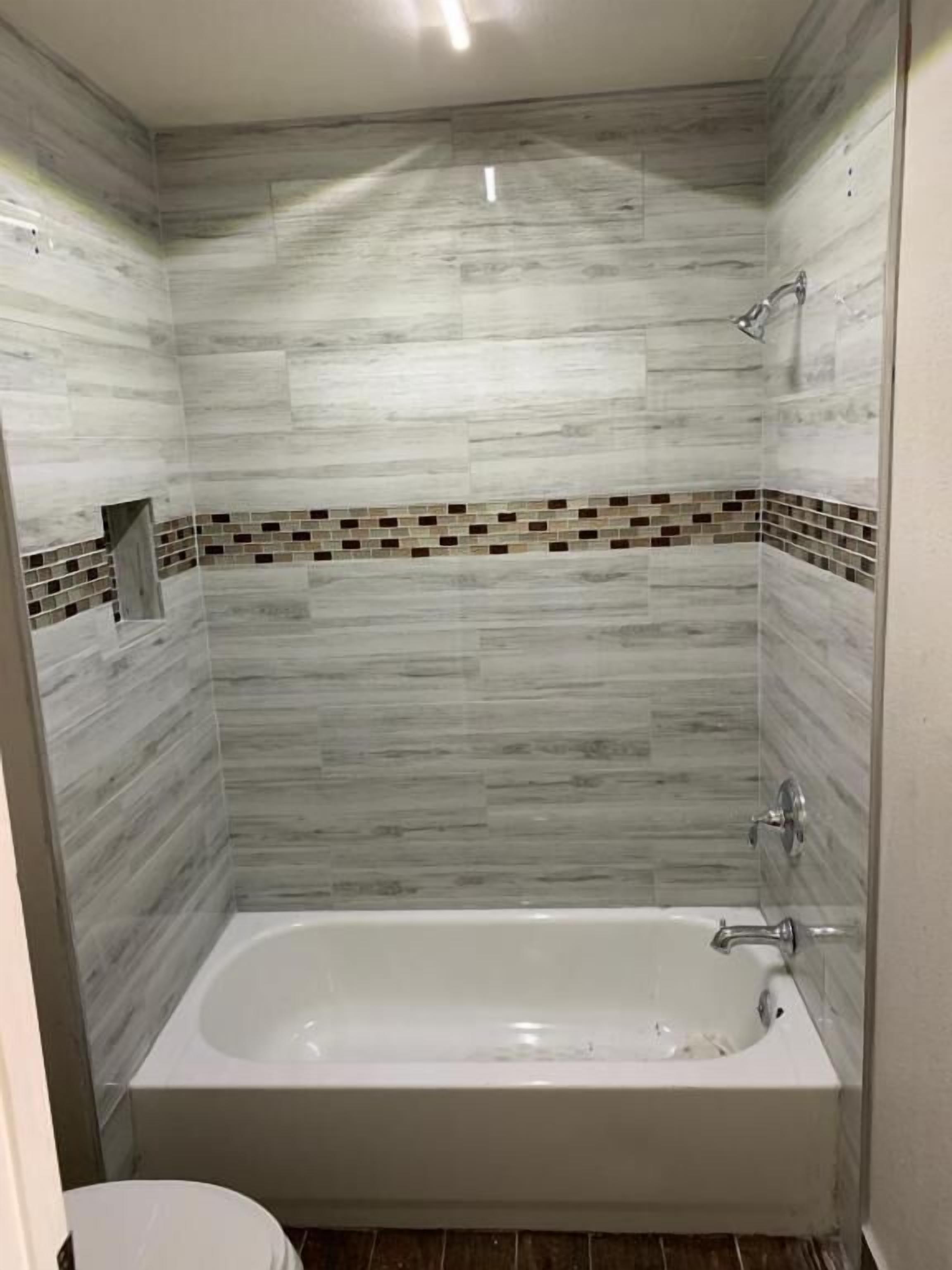 Un baño con bañera, paredes de azulejos y zona de ducha.