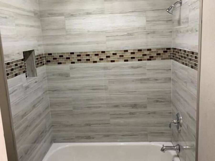 Un baño con bañera, paredes de azulejos y zona de ducha.