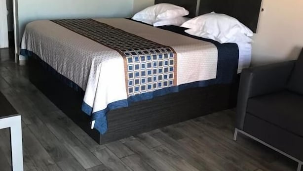 A bedroom with a bed, a nightstand, a chair, and a picture on the wall. - SouthTown SA Inn (San Antonio)