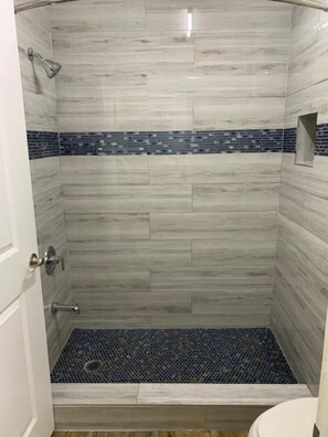 A shower with a tiled floor and a blue tile border.