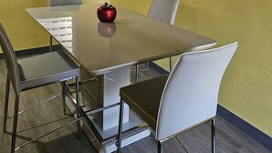 Een vergaderruimte met een witte tafel, vier stoelen, een rode appel op de tafel en een schilderij aan de muur.