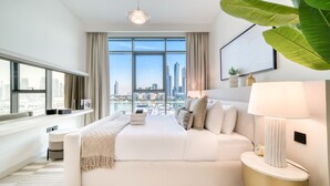 Een moderne hotelkamer met een groot bed, een nachtkastje met een lamp, uitzicht op de stad door grote ramen en een klein bijzettafeltje.