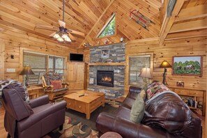 L’intérieur d’une cabane en rondins, avec une cheminée, des meubles en cuir et un téléviseur.