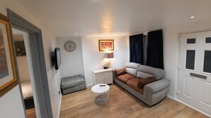 Un salón moderno con un sofá, una mesita redonda, un banco gris, un reloj y un cuadro en la pared.