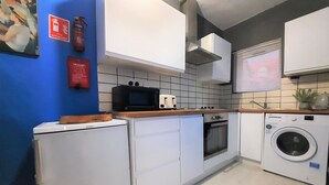 Cocina compacta con armarios blancos, microondas, tostadora, horno y lavadora.