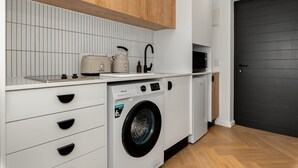 A compact kitchen with a washing machine, wooden cabinets, and a black door.