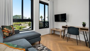 A modern living room with a grey sofa, a wooden desk, and a TV mounted on the wall.
