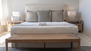 Un lit bien fait, avec une tête de lit, deux tables de chevet avec des lampes et un banc placé devant le lit.