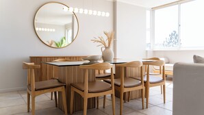 Un espace repas moderne avec une table ronde, six chaises en bois, un grand miroir et un vase contenant des plantes séchées.