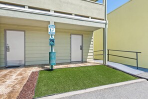 A pet waste station with a sign, a green artificial lawn, and a building with two doors.